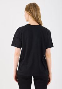 T-shirt de algodão preto com um corte descontraído, mangas curtas e decote redondo. As costas apresentam um design minimalista, sem logótipos ou enfeites.