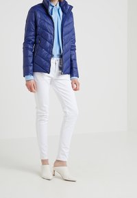 Marinblå vadderad jacka med quiltad design, parat med en blå- och vitrandig skjorta, vita slim-fit jeans och vita mules med en lätt klack.