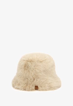 Chapeau seau en fausse fourrure beige clair, avec une texture douce, un dessus arrondi et une petite étiquette en cuir de marque sur le côté.