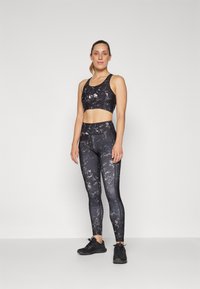 Sports bra and leggings set in black with a marble pattern. Smooth fabric, fitted design, and ankle-length leggings. Black athletic shoes.