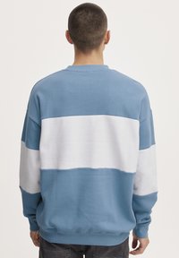 Pullover leggero blu chiaro e bianco con un design a blocchi di colore orizzontali. Maniche lunghe e polsini a coste, tessuto morbido, vestibilità casual.