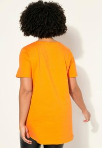 Orange kortærmet T-shirt i et blødt, let stof. Har en rund halsudskæring og en længere bagside med en glat tekstur.