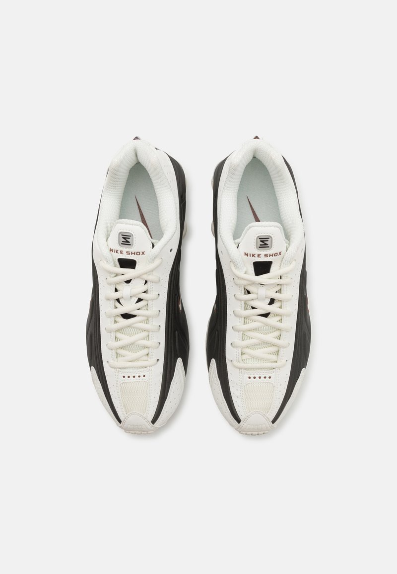 Nike Shox Sneaker mit einer atmungsaktiven, weißen Mesh-Oberfläche, schwarzen Akzenten, einem gepolsterten Kragen und einer auffälligen Dämpfungssohle mit sichtbaren Federn.