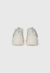 White sneakers with a textured mesh upper, silver accents, and chunky beige sole. Features a chain detail on the heel tab and logo tag.