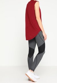 Punainen hihaton paita, jossa on kaareva helma, yhdistettyinä tiukasti istuviin harmaisiin legginsseihin, joissa on mustia paneeleja, sekä valkoisiin urheilukenkiin.