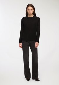 Maglione nero lavorato a maglia con maniche lunghe e texture a coste, abbinato a jeans grigi scuri a campana e scarpe nere con punta affilata.