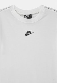 Biela bavlnená tričko s okrúhlym výstrihom, krátkymi rukávmi a čiernym logom Nike na hrudi. Malé čierne akcenty pozdĺž ramenného švu.