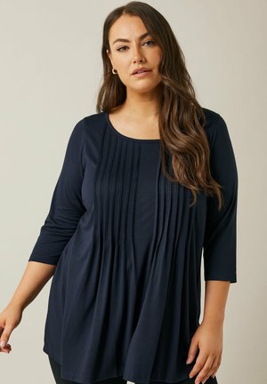 Top plisado azul marino con cuello redondeado y mangas tres cuartos. Tejido suave con un ajuste relajado y una textura sutil.