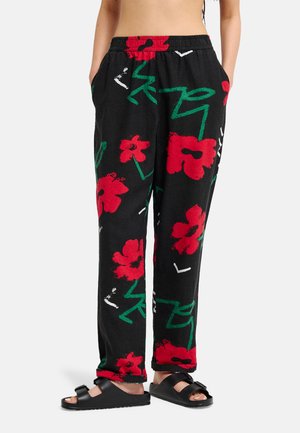 Zwarte loszittende broek met grote rode bloemenprints en groene abstracte stengels, gedragen met zwarte open-toe slip-sandalen.