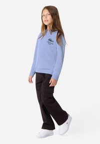 Felpa con cappuccio azzurra chiara con logo Lacoste nero, abbinata a pantaloni cargo neri e sneakers bianche. Look casual e comodo.