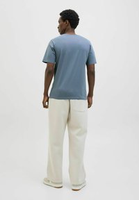 Blauwe t-shirt met korte mouwen, ontspannen pasvorm, gecombineerd met crèmekleurige wijde broek. Het materiaal lijkt zacht, met een minimalistisch ontwerp en een back pocket-detail.
