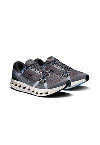 Zapatillas deportivas con parte superior de malla gris, acentos negros y suela blanca con agujeros de ventilación. Cuerdas delgadas y detalles decorativos en azul.