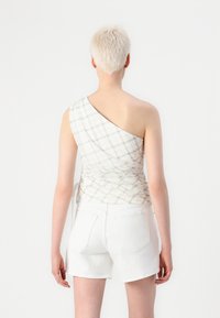 One-shoulder top in light plaid pattern with ruched texture and side ties, paired with white denim shorts.