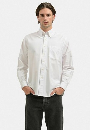 Hvid skjorte med knapper og klassisk krave, lange ærmer, brystlomme og en glat tekstur, parret med mørke jeans.