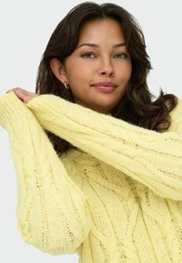 Pull en tricot jaune clair avec un motif en relief, des manches larges et une coupe décontractée. Gros plan mettant en avant la douceur du pull.