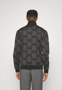 Chaqueta negra con un intrincado patrón gris, cuello alto y puños acanalados. Presenta una textura suave y un ajuste relajado.