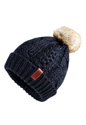 Bonnet d'hiver en tricot bleu foncé avec un revers côtelé plié, un pompon en fausse fourrure sur le dessus et une petite étiquette en cuir marron sur le revers.