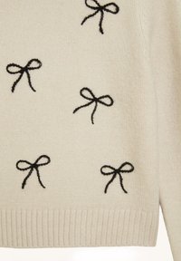 Maglione color crema con fiocchi neri ricamati, caratterizzato da orlo a costine e materiale lavorato a maglia testurizzato. Design casual con motivo a fiocchi ripetuti.