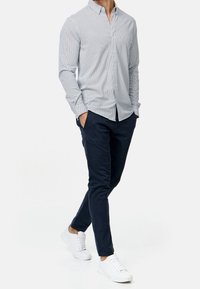 Světlomodrá košile na knoflíky s malým námořnickým vzorem, doplněná námořnickými kalhotami a bílými teniskami. Přiléhavý střih, bavlněný materiál, dlouhé rukávy.