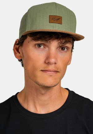 Grüne Mütze mit Fischgrätmuster, braunem Lederpatch und hellbraunem Schirm. Getragen mit einem schwarzen T-Shirt. Einfaches Design, lässiger Look.