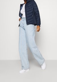 Granatowa kurtka puchowa z kapturem, dopasowany biały top, jasnoniebieskie luźne dżinsy i białe trampki. Strój charakteryzuje się casualowym, ale wygodnym stylem.