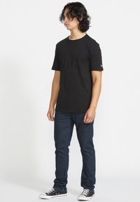 Sort bomulds t-shirt med rund hals og korte ærmer, der har en brystlomme. Sammen med blå denimjeans og sorte sneakers.