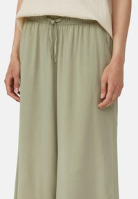 Pantalons larges vert clair en tissu doux avec une taille à cordon et des poches latérales. Texture lisse avec une coupe décontractée.