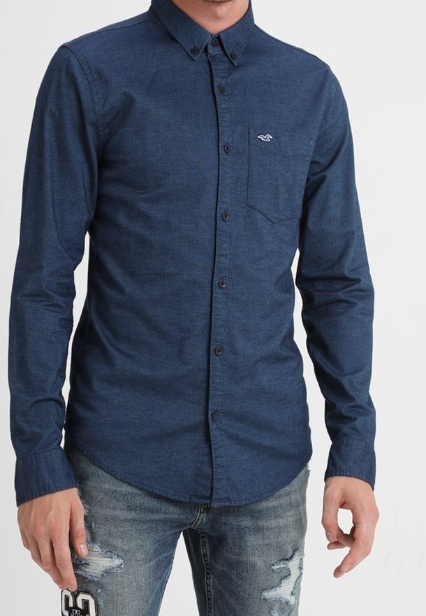 Námořnická modrá košile na knoflíky z texturované látky, s kapsou na levé hrudi a logem. V kombinaci s ošuntělými džíny.