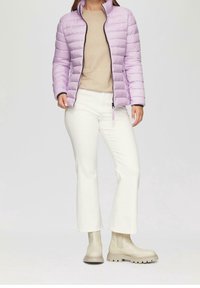 Veste matelassée violet clair avec couture horizontale, fermeture éclair noire, haut beige, pantalon blanc évasé et bottines beige avec semelles épaisses.