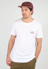 T-shirt en coton blanc à manches courtes et col rond ; présente un petit graphisme orange et bleu sur le côté gauche de la poitrine.