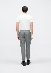 Szürke munkásnadrág gumis derékrésszel, oldalzsebekkel és szűkített szárakkal, egyszínű fehér pólóval és fekete lábbelivel párosítva.