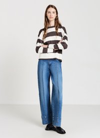 Striped sweater in brown and white, ribbed texture, paired with wide-leg blue jeans with visible seams and a slight flare at the hem. Black shoes.