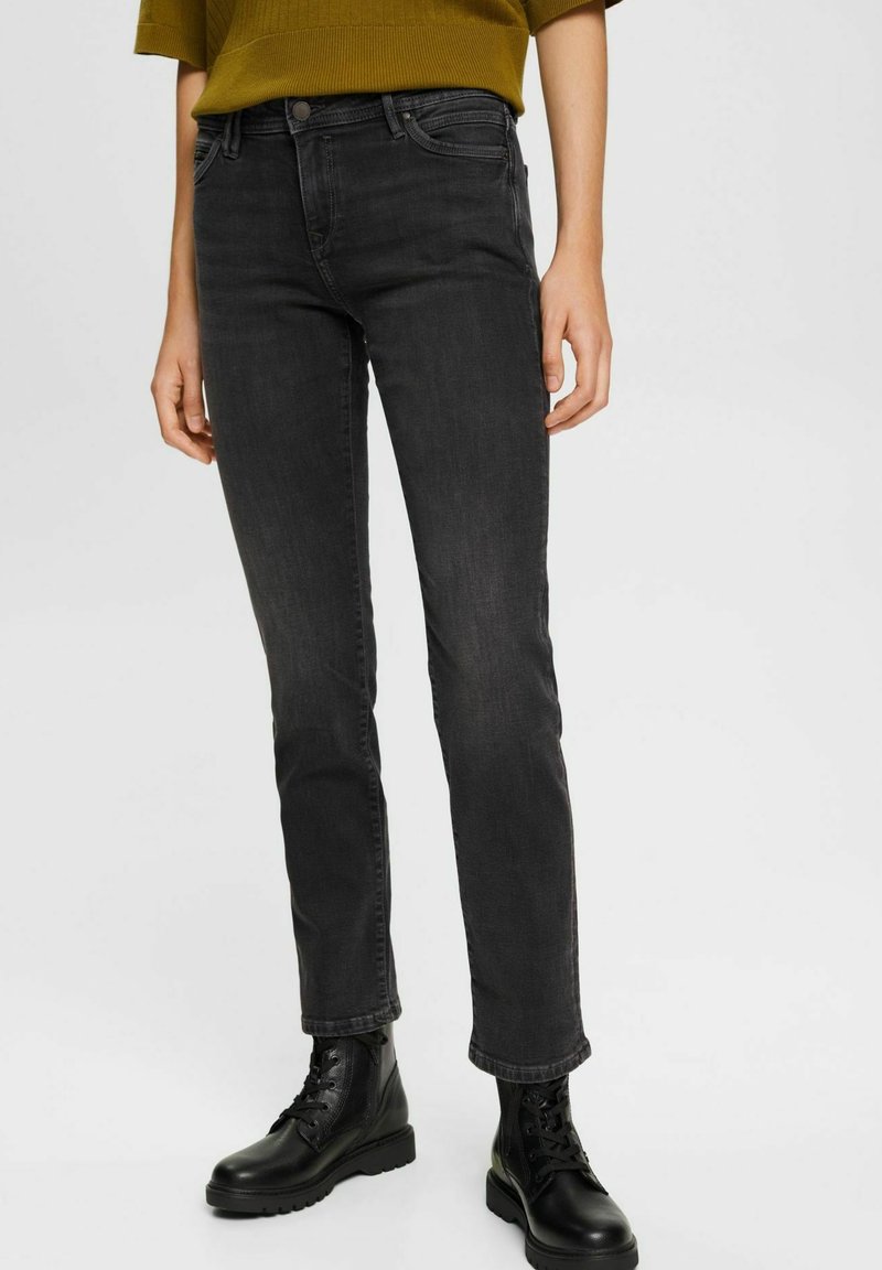 Jeans noirs à jambe droite en denim avec une texture légèrement usée. Associés à des bottes à lacets noires et un top vert à manches courtes.