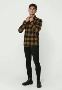 Pruun ja merevä värviga ruuduline flanellist särk pikkae varrukatega ning nööbiga kinnitamine, koos mustade kitsaste pükste ja mustade madala kontsaga saapastega.