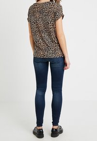 Halenka s krátkým rukávem a leopardím potiskem volnějšího střihu, spojená s tmavě modrými Skinny džínami a černými botami. Hladký materiál, ležérní design.