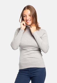 Maglione grigio a collo alto in una vestibilità aderente, realizzato in tessuto morbido, con maniche lunghe e una texture liscia, abbinato a jeans denim scuri.