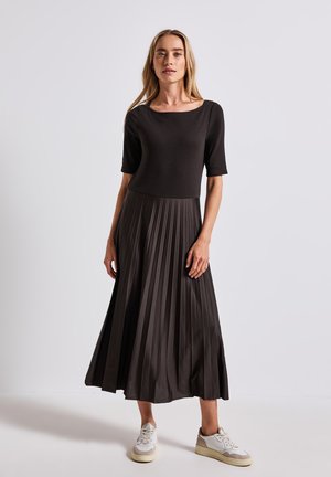 Schwarzes, plissiertes Midikleid mit U-Boot-Ausschnitt und kurzen Ärmeln, aus glattem Stoff, kombiniert mit weißen Sneakers.