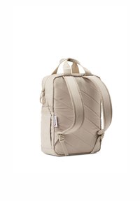 Beige gesteppter Rucksack mit zwei Tragegurten, verstellbarem Schnallenverschluss, Oberhandgriff, Seitentasche und einem Markenetikett. Glatte Textur, rechteckige Form.