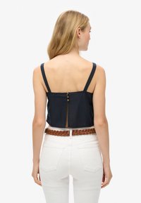 Marineblauw crop top met dikke banden, een knoopsluiting op de rug en een iets doorzichtige paneel. Gepaard met witte high-waisted jeans en een gevlochten riem.