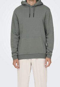 Sweat à capuche vert olive en tissu doux, doté d'une poche avant, d'une capuche avec cordon ajustable, et de poignets et ourlet côtelés.