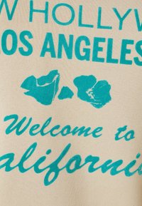 Tessuto beige con testo grafico turchese "NEW HOLLYWOOD LOS ANGELES" e "Benvenuto in California", accompagnato da due design stilizzati di fiori.