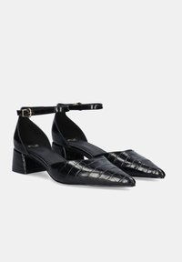 Zapatos de tacón de piel sintética negra con tiras al tobillo y patrón de cocodrilo, punta afilada y tacón bajo para mayor estabilidad. Presenta una tira delgada para un ajuste seguro.