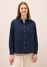 Denimskjorta i mörkblått, med knappstängning fram, två bröstfickor och långa ärmar. Mjuk textur med en avslappnad passform.