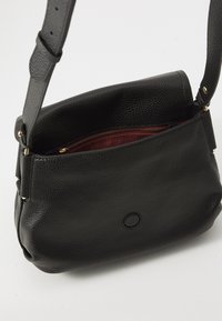 Borsa a mano in pelle nera con superficie texturizzata, forma morbida, tracolla regolabile e rivestimento rosso con tasca con zip all'interno.
