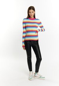 Maglione multicolore a coste con strisce blu, rosa e gialle, abbinato a pantaloni neri lucidi e sneaker multicolori.