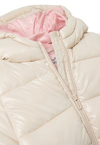 Giubbotto imbottito con un esterno lucido di colore crema e fodera rosa. Presenta una chiusura con zip e un design trapuntato con cuciture in evidenza.