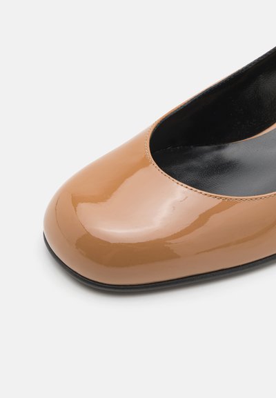 Beige kiilakuvioinen patentoitu nahkainen balettikenkä, jossa on pyöreä nenä ja sileä, kiiltävä pinta. Musta sisävuori ja vähäiset ompeluyksityiskohdat.