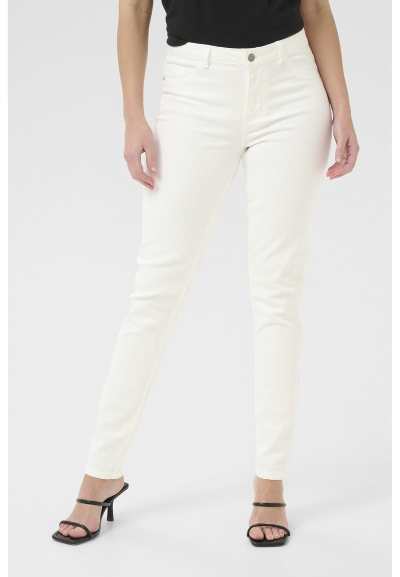 Jeans blancs ajustés avec une texture lisse, dotés d'une fermeture à boutons à l'avant et de poches arrière, associés à des talons ouverts noirs.