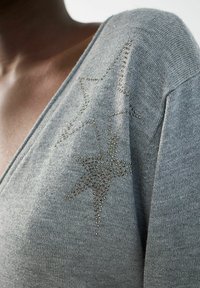 Grijze V-hals trui van zacht tricotmateriaal, met decoratieve sterontwerpen versierd met kleine strass steentjes op één schouder.
