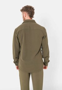Camicia a maniche lunghe verde oliva con colletto, polsini abbottonati e una texture liscia. Il retro presenta una cucitura a yoke e un orlo leggermente curvato.